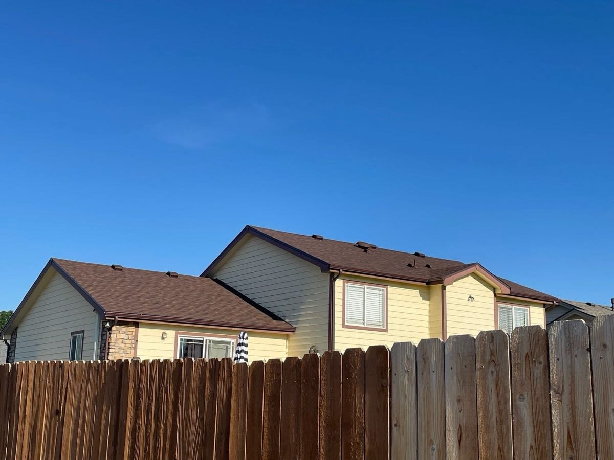 Two neighboring homes with newly completed brown shingle roofs under a clear sky