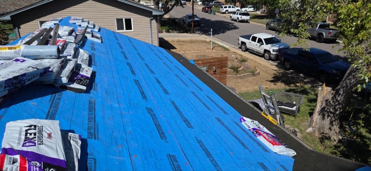 Roof deck covered in blue synthetic underlayment with shingle bundles staged for install