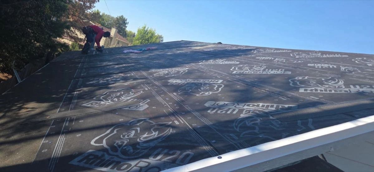 Crew member rolling out synthetic underlayment on a stripped roof deck