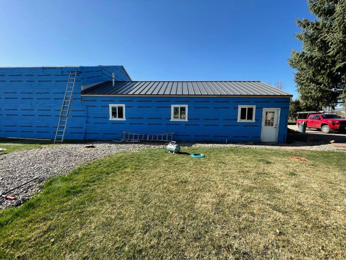 Shop building wrapped in house wrap with a new dark metal roof in place